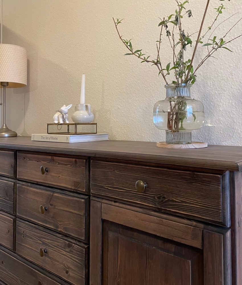 Trækommode med lampe, bog, og vase med grene i en moderne indretning